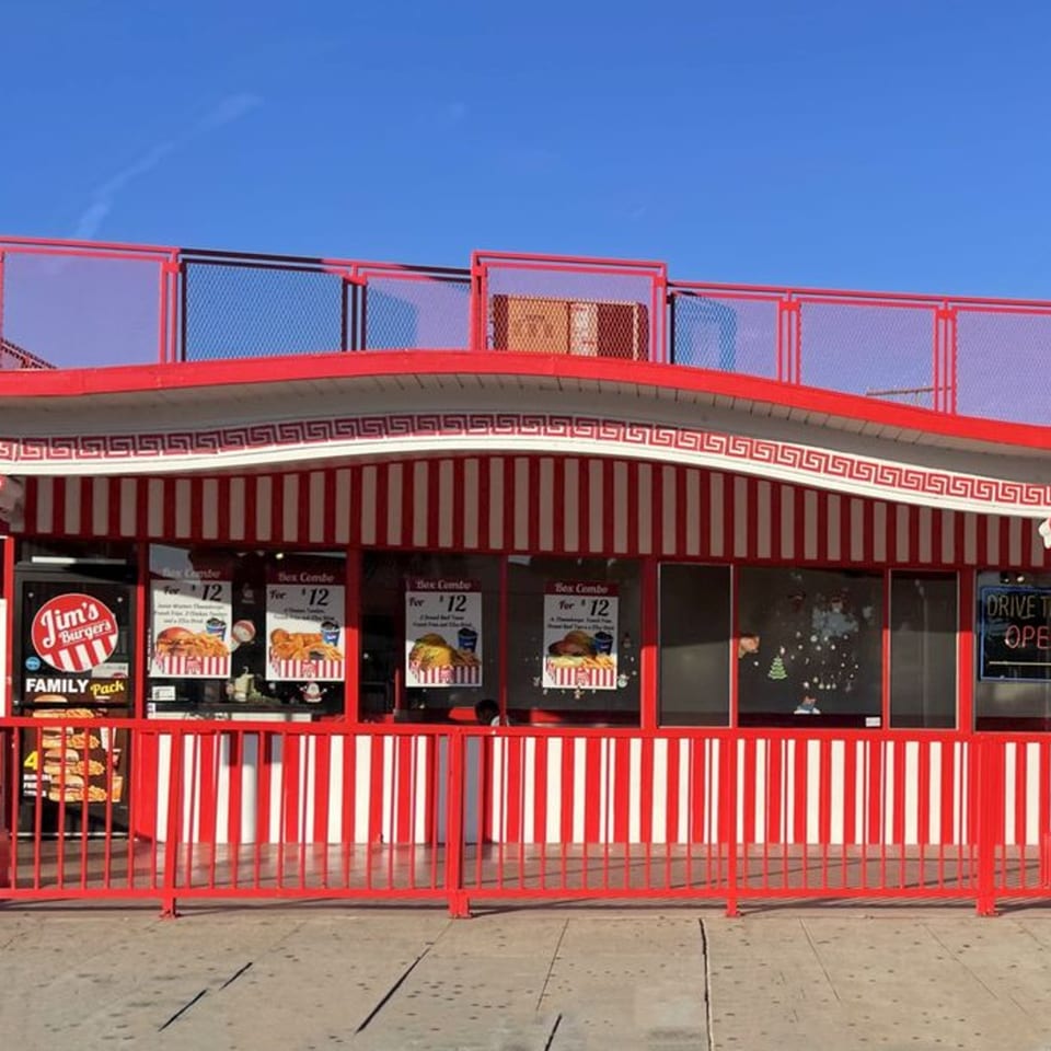 Jim's Burgers restaurant exterior with red and white striped awning and red fencing under a blue sky.