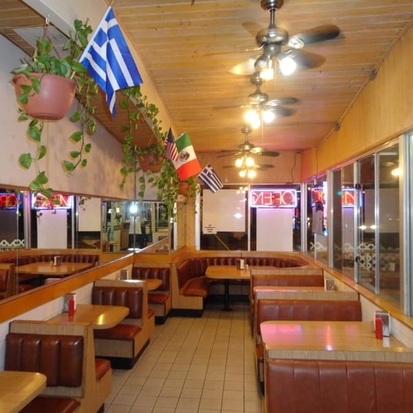 Interior of Jim's Burgers showing empty brown booths, wooden tables, ceiling fans, and flags.