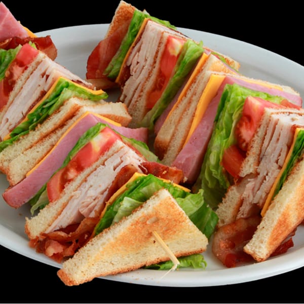 A white plate filled with several club sandwiches, cut into triangles, showing layers of meat, cheese, and vegetables.
